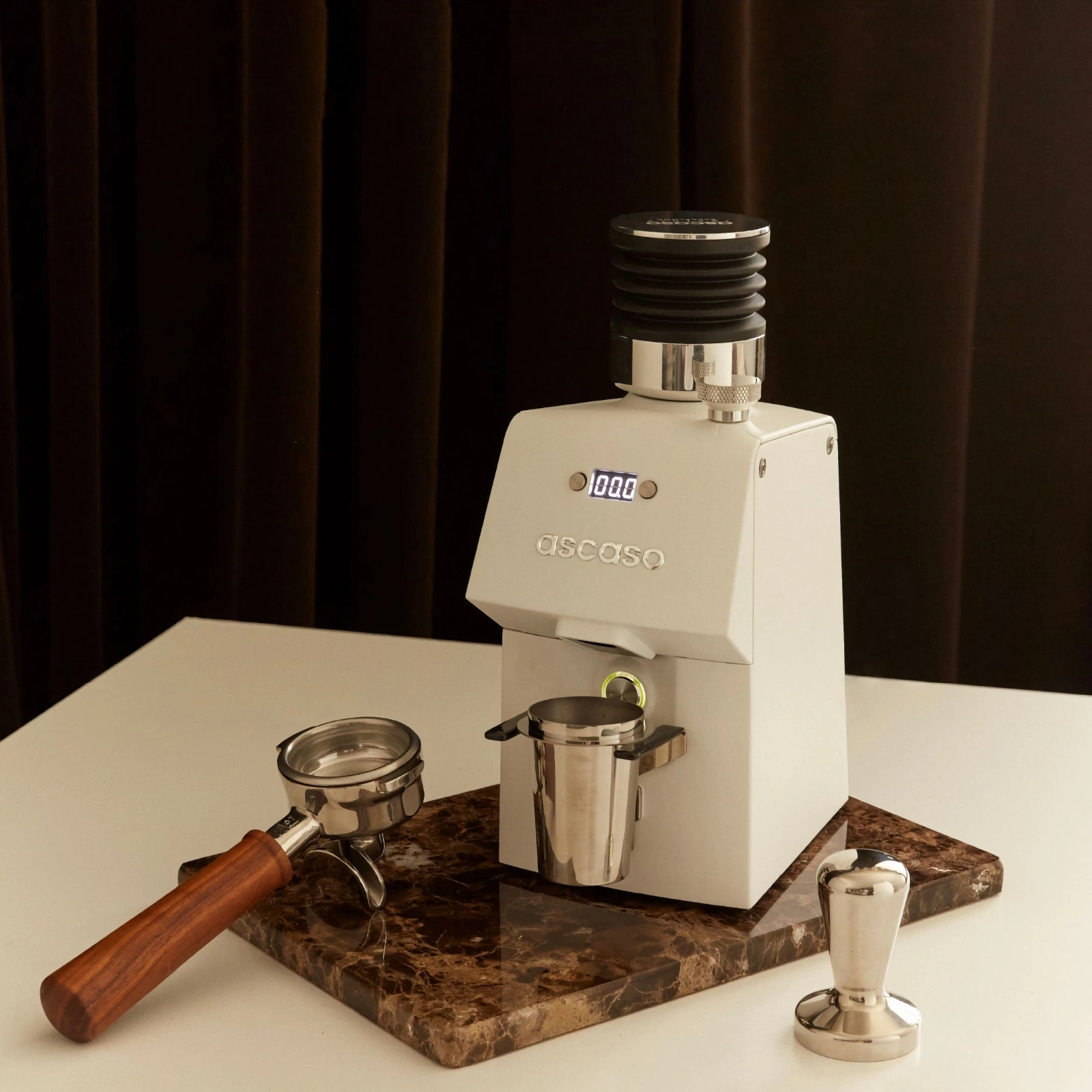 Белая „Ascaso“ H64 с бункером „Single Dose“ и дозировочной чашкой, рядом — портафильтр и темпер