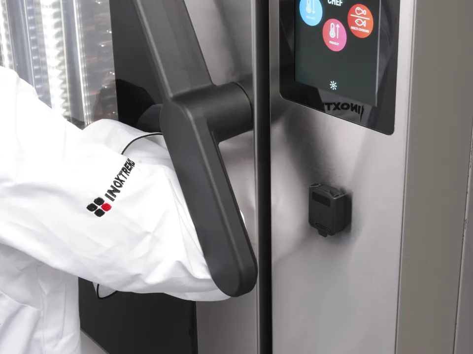 Повар открывает дверцу печи „Inoxtrend“ Flexo локтем за эргономичную ручку